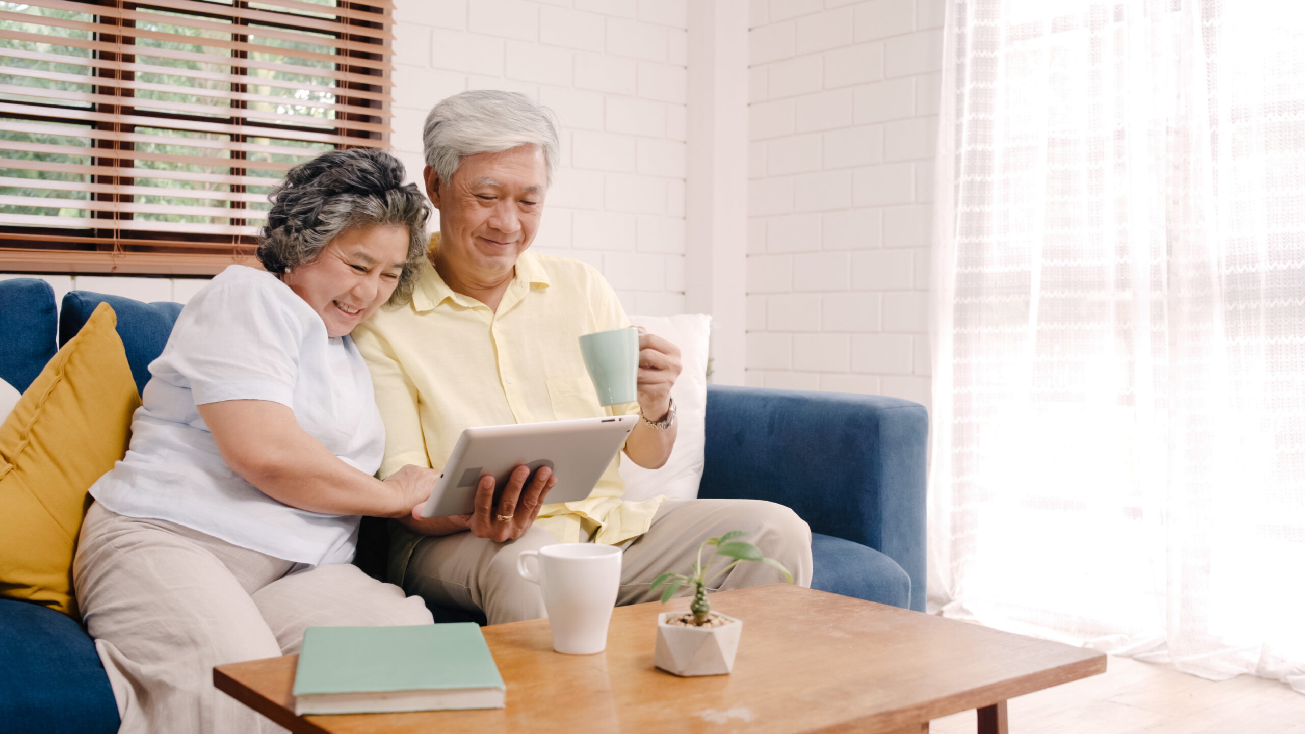 Asian elderly couple using tablet and drinking coffee in living