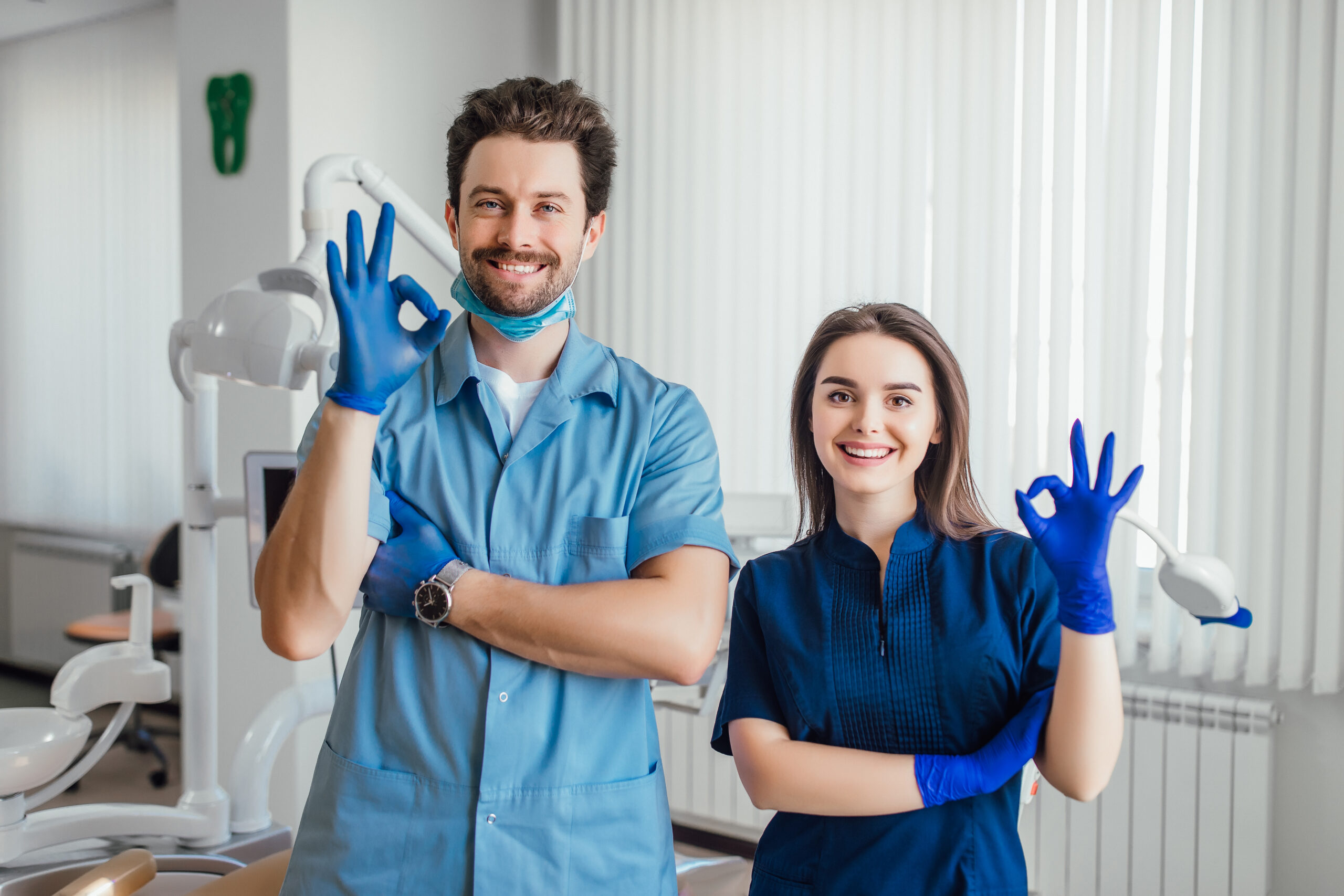 photo-of-smiling-dentist-standing-with-arms-crossed-with-her-colleague-showing-okay-sign