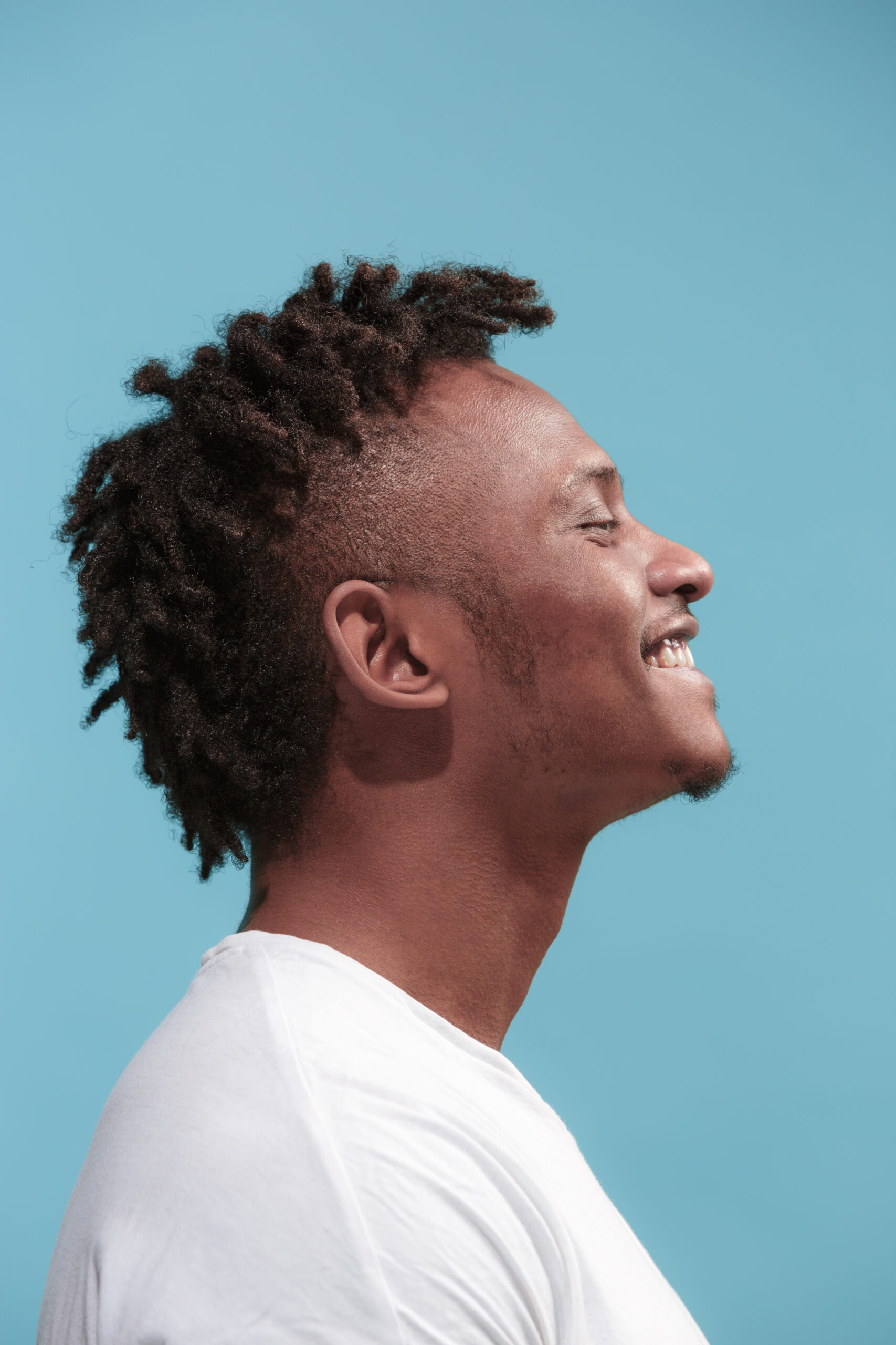 The happy business Afro-American man standing and smiling against blue background. Profile view.