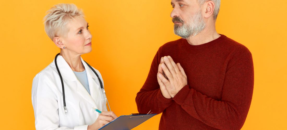 Sad frustrated elderly male with beard pressing hands together asking his female doctor to cure him from respiratory disease during physical examination, talking about symptoms. People, age and health